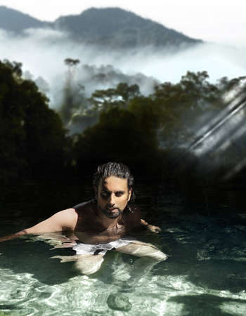 Man bathing in tropical waters with beautiful forests and mountain in the backgroundの写真素材
