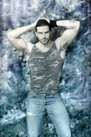 Stylized outdoor portrait of muscular man posing in tank top and jeans against winter wonderland...