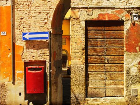 Scene of an ancient wall in Europe (Italy) featuring blue traffic arrow, red post box, and weathered stone and wood の写真素材