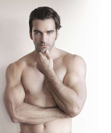 Shirtless young man with hand to chin against neutral backgroundの写真素材