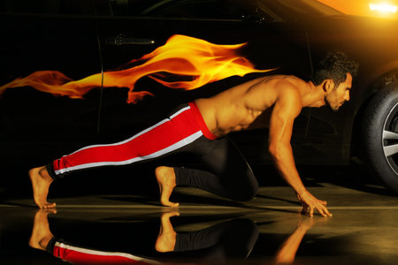 Concept photo of a young muscular athlete posed ready to run with car and flame behind him