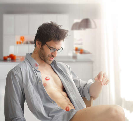 Portrait of sexy man at home with shirt open and lipstick kiss marks on his bare body and playful fun expressionの写真素材