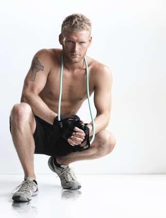 Sexy serious young man athlete crouched down with jump rope around his neckの写真素材