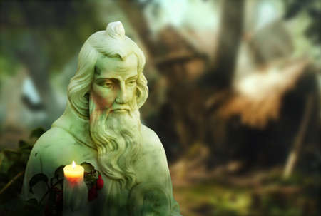 Very old religous statue in garden setting with burning candleの写真素材
