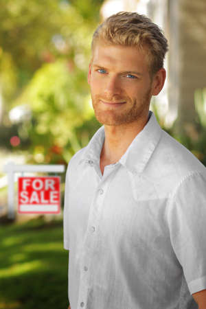 Young attractive man outdoors in front of "for sale" home signの写真素材