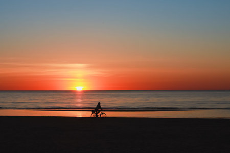 Silhouette of a cyclist on the beach at sunsetの写真素材