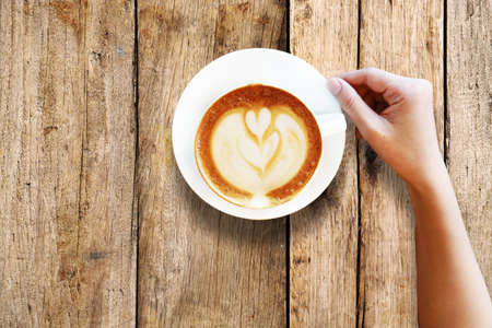 Hand holding a cup of coffee on wooden tableの写真素材
