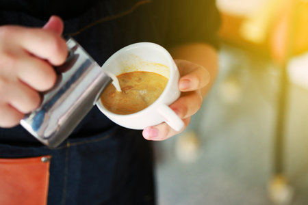 Barista hands pouring warm milk in coffee cup for making latte art. Multi skill of barista to make coffee drink in coffee shop. Professional in hot and cold drinkの写真素材
