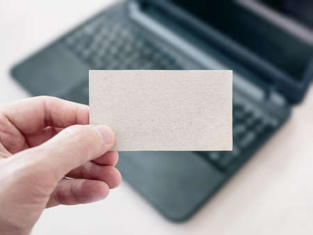 Man Holding a Blank Cardboard Business Card and Using Modern Laptopの写真素材