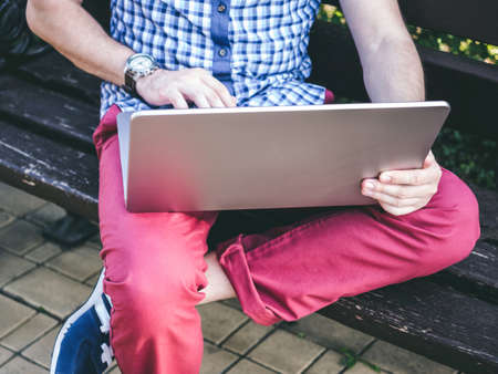 Young Man Sitting On Park Bench and Working On His Laptopの写真素材