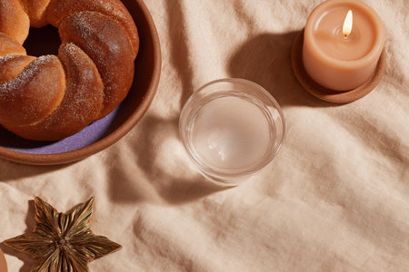 A traditional Rosca de Reyes bread on a clay plate, accompanied by a glass of holy water and a lit candle. The setting reflects Three Kings Day celebrations.の素材