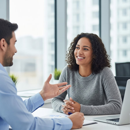 Smiling businesswoman sitting at desk and talking with colleague in officeの素材