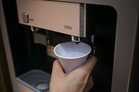 A hand holding a paper glass for cold clean water; for drinking, from hot and cold water machine.の写真素材