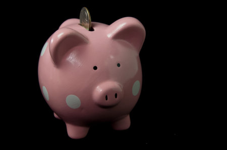 Pink Polka Dot  PIggy Bank with coin in slot on back backgroundの写真素材