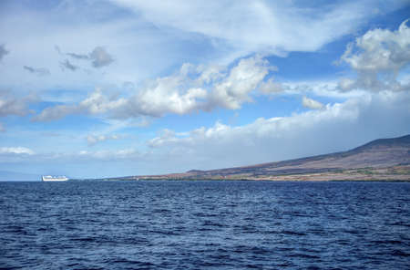 Scenic clouds with small white cruise ship and Maui mountins in backgroundの写真素材