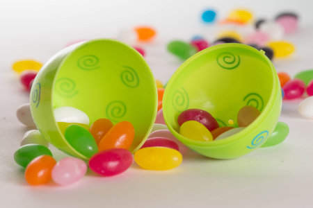 Decorated plastic Easter egg open with colorful jelly beans out of focus in background. Isolated on...