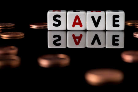 Save spelled in dice letters reflected on isolated black background with scattered pennies out of focusの写真素材