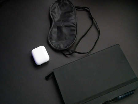 Fashion concept : Flat lay of black notebook, Black mask for sleep and wireless headphones on black backgroundの写真素材