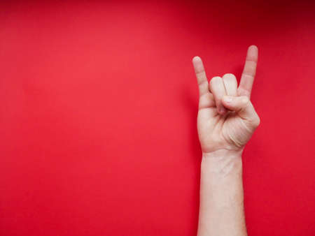 Female hand shows a gesture of rock (horns) on red backgroundの写真素材