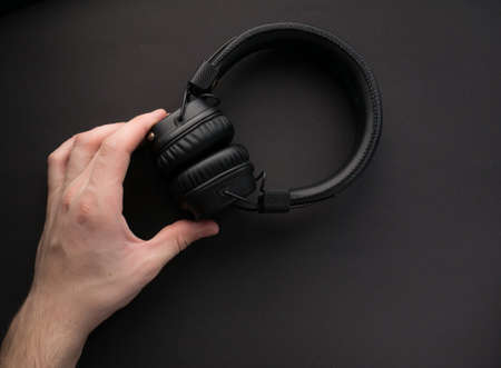 Classic black wireless headphones on colored paper background. Retro style. 80s. Pop culture. Top view. Minimal Music Concept. Hands holdingの写真素材