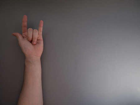 Female hand shows a gesture of rock horns on gray background. Copy space for your text.の写真素材