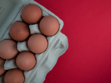 Overhead view of brown chicken eggs in an open egg carton isolated on red. Fresh chicken eggs background. Top view with copy space. Natural healthy food and organic farming concept. Eggs in boxの写真素材
