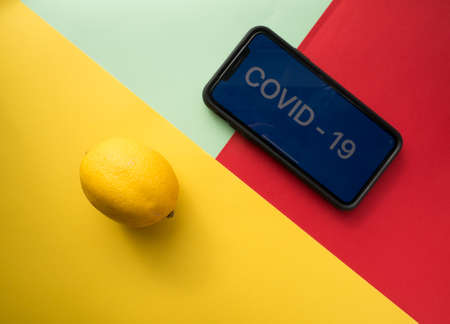 USA, March 16, 2020. Lemon and smartphone with the inscription COVID - 19 on a colored background. Vitamin C. The concept of treatment of the virus. Top viewのeditorial素材