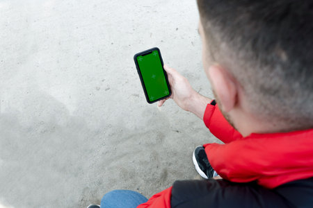 Male hand holding smartphone with green display for your content, man's hand using cellphone with...