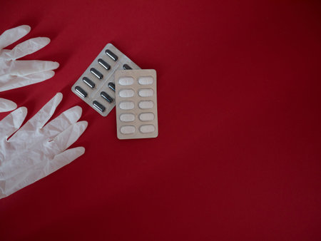 Close up of vitamin pills and white latex glove on red background. One of the ways to reduce the...