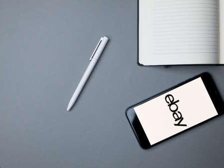 USA - May, 2020; Ebay Iphone Application Screen with pen and notebook on gray paper background.のeditorial素材