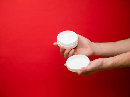 Male hand holding unbranded plastic tubewith white cream. Flacon for cream, toiletry. Bottle for professional cosmetics product. Skincare and beauty concept. Mockup, copy space. Isolated on red.の写真素材
