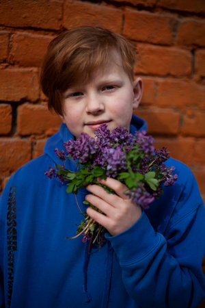 Boy with red hair and a blue sweatshirt with a bouquet of purple wildflowersの写真素材