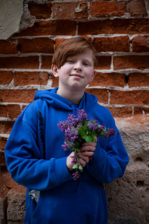 Boy with red hair and a blue sweatshirt with a bouquet of purple wildflowersの写真素材