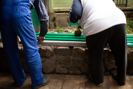 Two workers paint a park bench in green