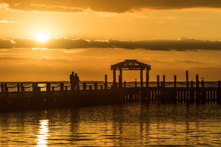 A couple watches a yellow sunset over Brnegat Bay from Long Beach Island at the Jersey shoreの写真素材