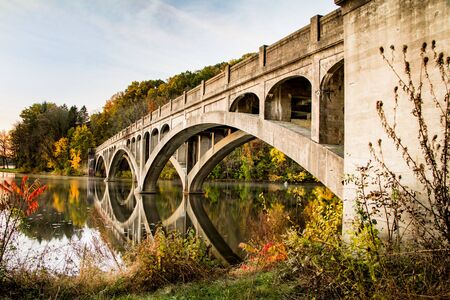 Arched cement bridge over Lake Ontelaunee closed to traffic pictured against fall foliageの写真素材