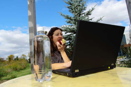 Woman eating apple outside at the computer の写真素材