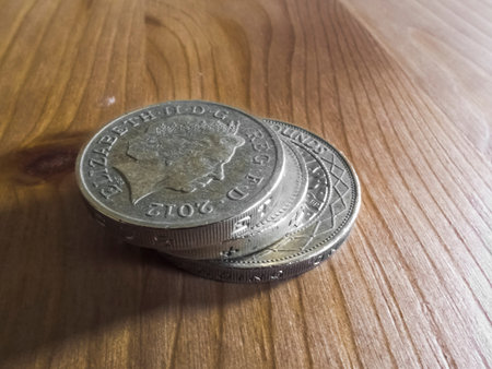 A stack of British Pound coins (Great British Pounds Sterling) on a wooden table.