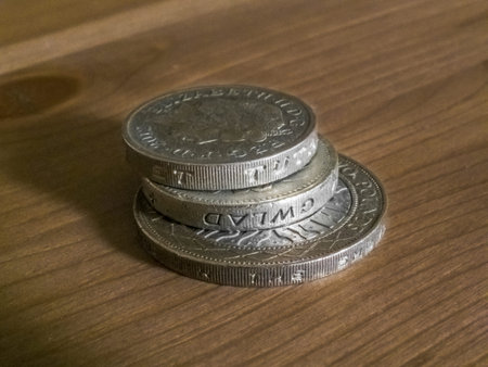 A stack of British Pound coins (Great British Pounds Sterling) on a wooden table.