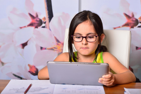 Little cute girl using at home a Tablet PC for homeworkの写真素材