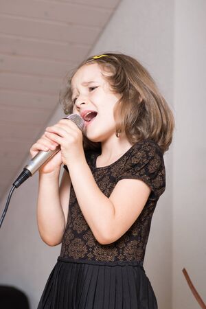 Little cute girl singing karaoke on microphone at homeの写真素材