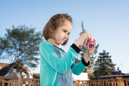 Little cute girl taking photos in the garden with a camera
