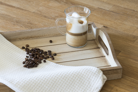 Glass of latte macchiato and coffee beans on a wooden trayの写真素材
