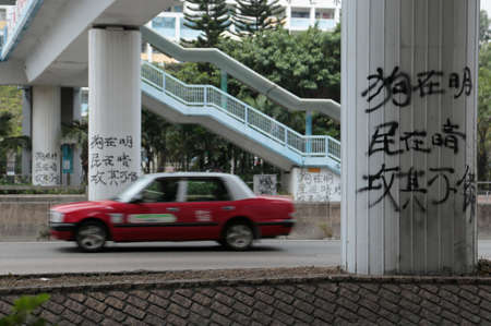 A taxi drive passes a pedestrian bridge painted with protest graffiti in Hong Kongのeditorial素材