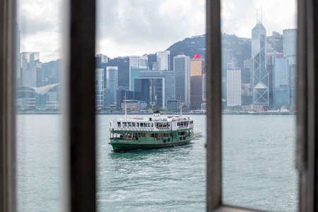 Star Ferry's ferry is seen through from a window of passenger waiting area, as it navigates across the strait between Tsim Sha Tsui Star Ferry Pier to Victoria Harbour of Hong Kong Islandのeditorial素材