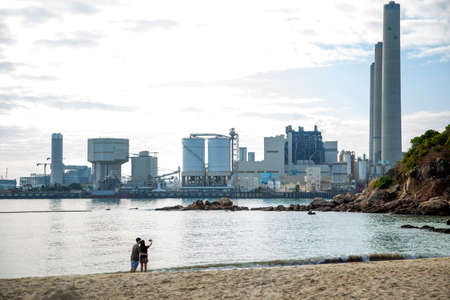 A couple take selfie photos on a beach near the electricity plant of Lamma Island, Hong Kong.のeditorial素材