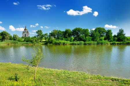 Romantic churchand lake on green grassland under blue sky. Ukraine.
