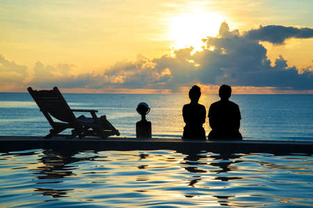 couple sit at swimming pool watching sunset at seaの写真素材
