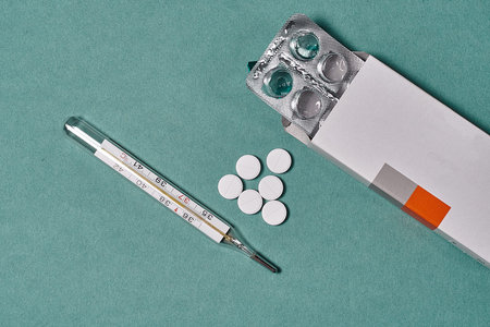 Packaging with tablets and a thermometer on a light background, top view. Free space, possibility of...