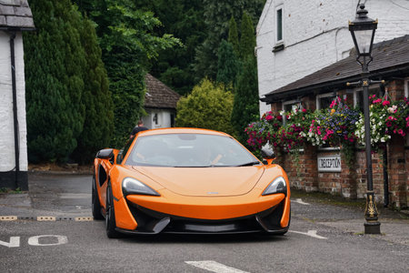 Bright orange sports car parked in a charming village with flower-adorned buildings in the...